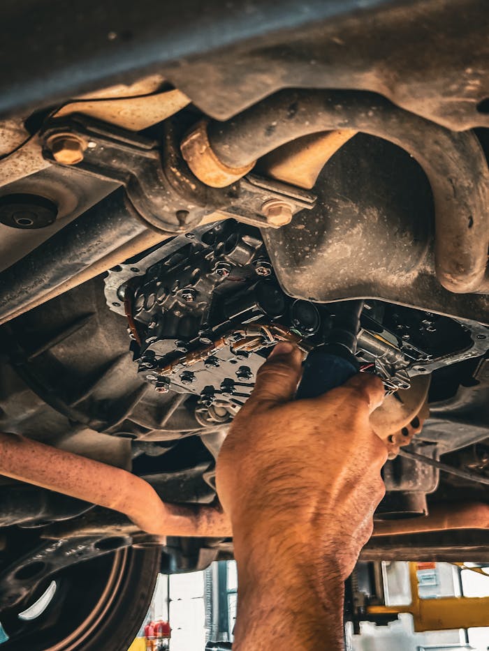 Mechanic working on car undercarriage in a garage setting.